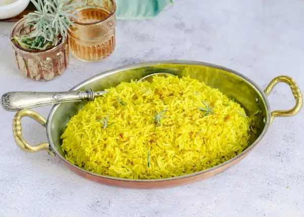 Un aromático arroz al curry, teñido de un vibrante amarillo por la cúrcuma y decorado con hebras de azafrán y romero fresco.