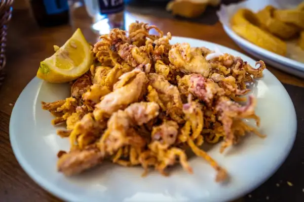 Plato de puntillas de calamar fritas, crujientes y doradas, servido con una rodaja de limón.