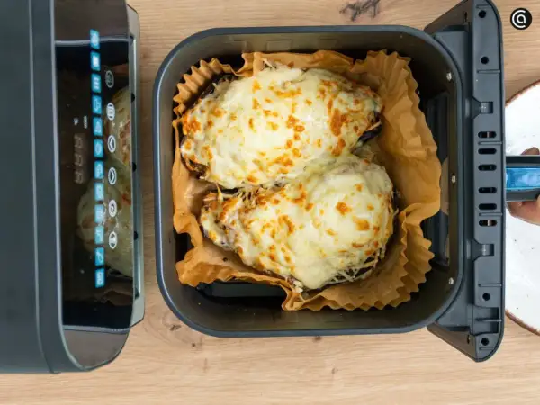 Dos berenjenas rellenas, cubiertas de queso derretido y dorado, listas para disfrutar tras su paso por la freidora de aire.
