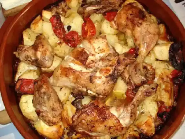 Rustidera de pollo dorada con patatas y pimientos asados, lista para servir.