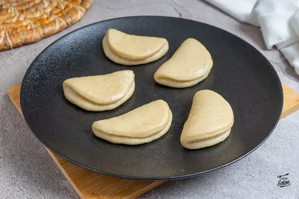 Cinco panes bao crudos en un plato negro, listos para la receta.