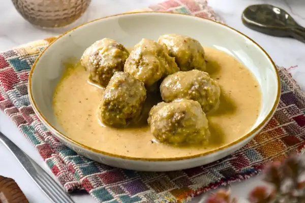 Deliciosas albóndigas en salsa de almendras, servidas en un plato sobre un mantel colorido.