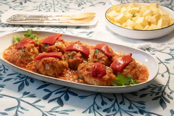 Sabrosos **rollos de bonito** en salsa de tomate, coronados con pimientos rojos. Acompañados de patatas fritas en un bol.
