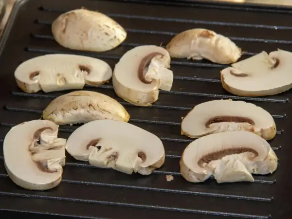 Champiñones cortados a la mitad y enteros sobre una parrilla, listos para deliciosas recetas con champiñones.
