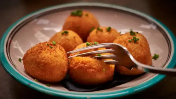 Croquetas de puchero doradas y crujientes, servidas en un plato con un tenedor listo para probarlas.