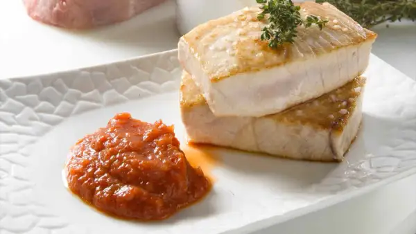 Dos jugosos trozos de atún a la plancha, con sal gruesa y una ramita de tomillo, acompañados de una porción de salsa de tomate casera.