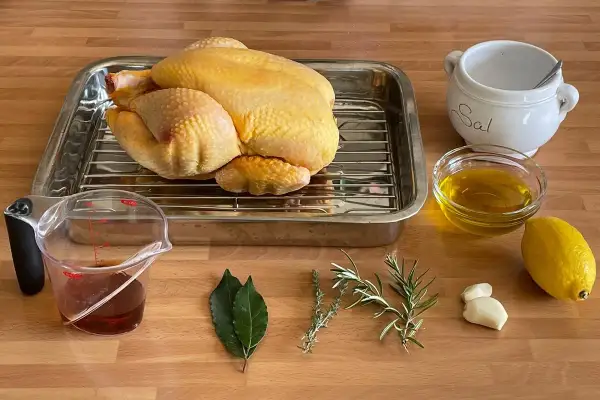 Un pollo crudo listo para asar, con ingredientes como limón, aceite, hierbas, ajo y sal. ¡Perfecto para un delicioso pollo al ast!