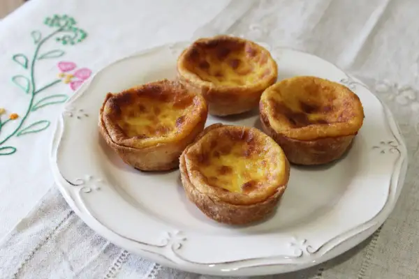 Cuatro deliciosos pastelitos de arroz con relleno cremoso y dorado, servidos en un plato blanco sobre un mantel bordado.