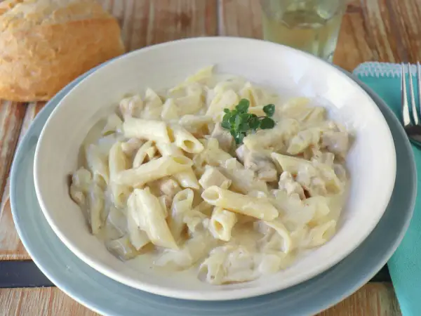 Un plato cremoso de macarrones con nata y trocitos de pollo, decorado con una ramita de tomillo.