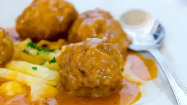 Albondigas a la jardinera, jugosas y cubiertas de salsa, acompañadas de patatas y perejil. Un plato casero listo para disfrutar.